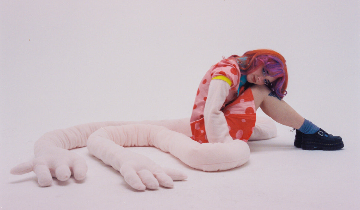 Sophie Truax wearing a brightly colored dress and sitting with the long arms from the 10 Feet Tall song/video